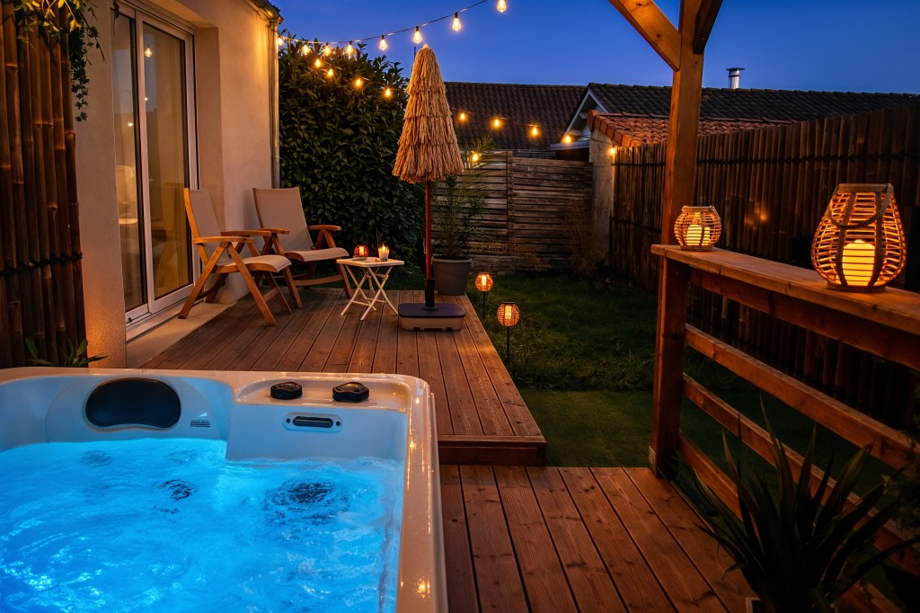 Jacuzzi extérieur privatif éclairé de nuit sur terrasse en bois avec guirlandes lumineuses à Angoulême